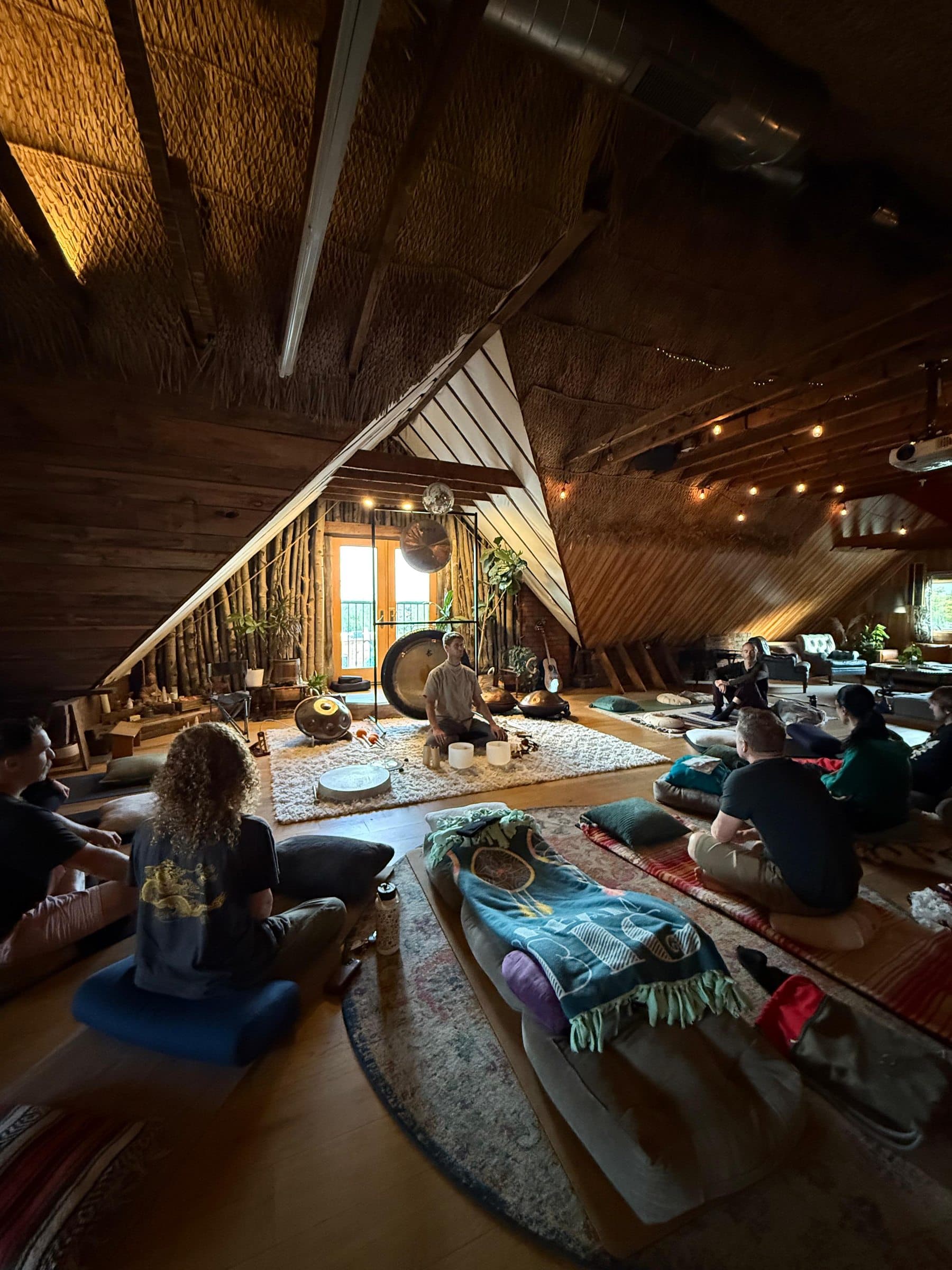 David facilitating a group sound journey in the timber A-frame space — participants on floor cushions, gong and handpans at the center
